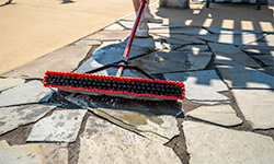 Large push broom with squeegee attachment being used to clean ice cubes off of a pool deck