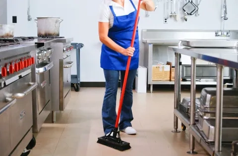 An image of a kitchen worker cleaning the floor with the Libman Heavy Duty brush.